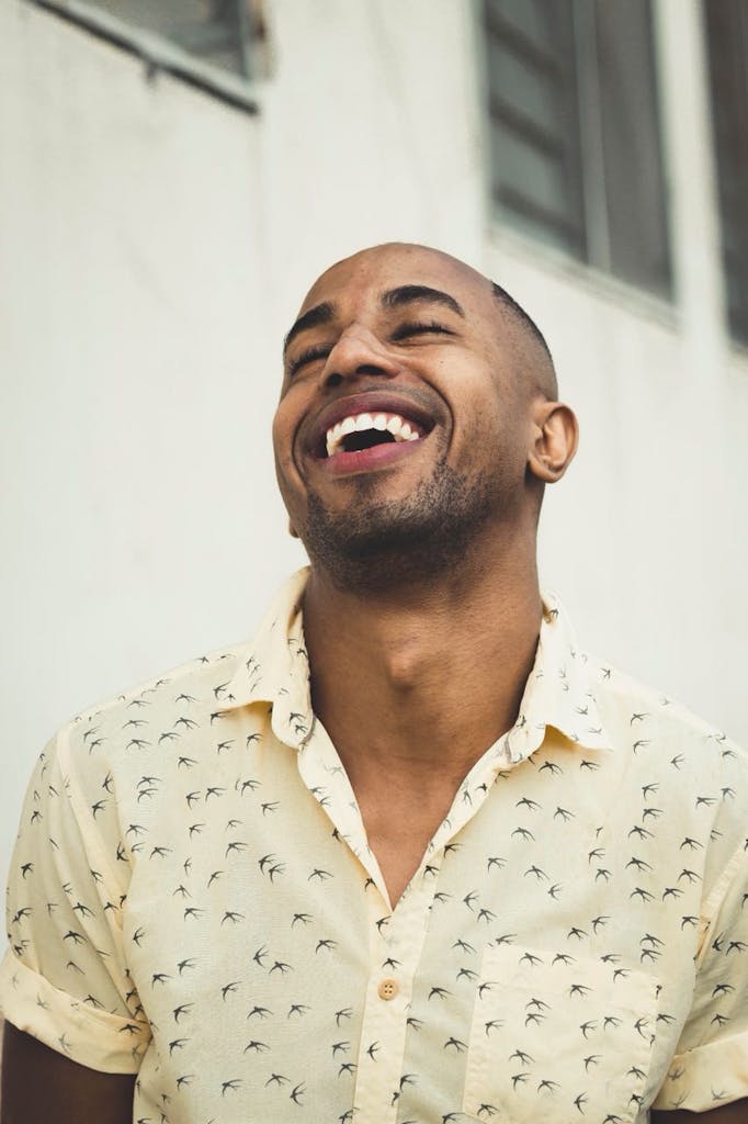 A cheerful man in a patterned shirt smiling joyfully outdoors.