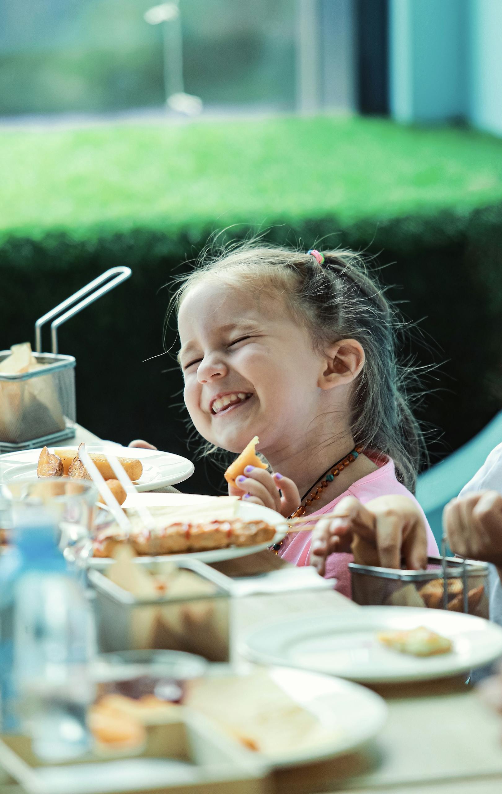 Happy girl enjoying a meal indoors, captured in vibrant lighting, smiling widely.